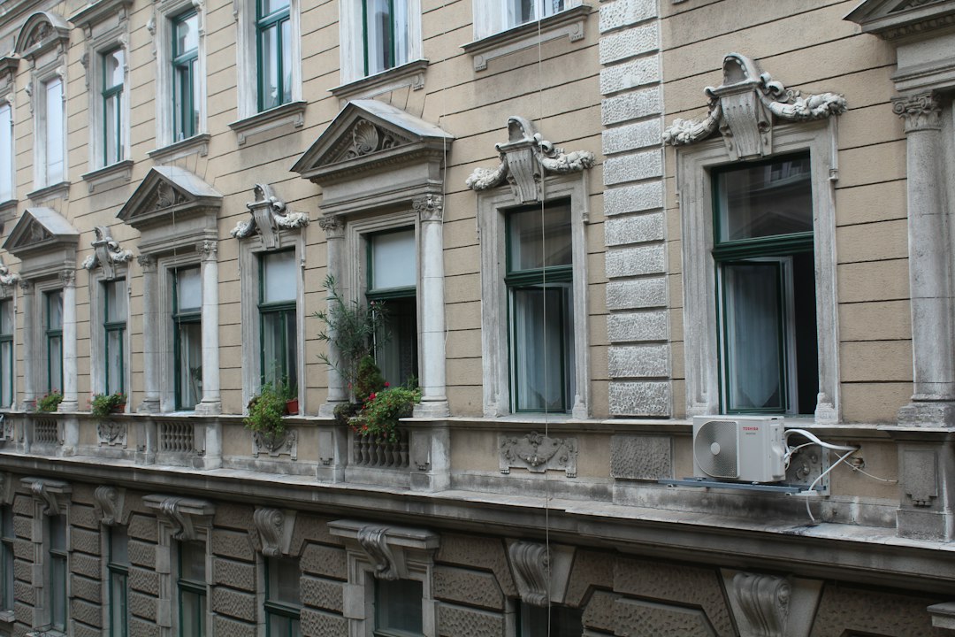 Fațadă de bloc cu tencuiala desprinsă și plasă de protecție montată pe schelă, cu zona de la bază delimitată cu bandă de avertizare